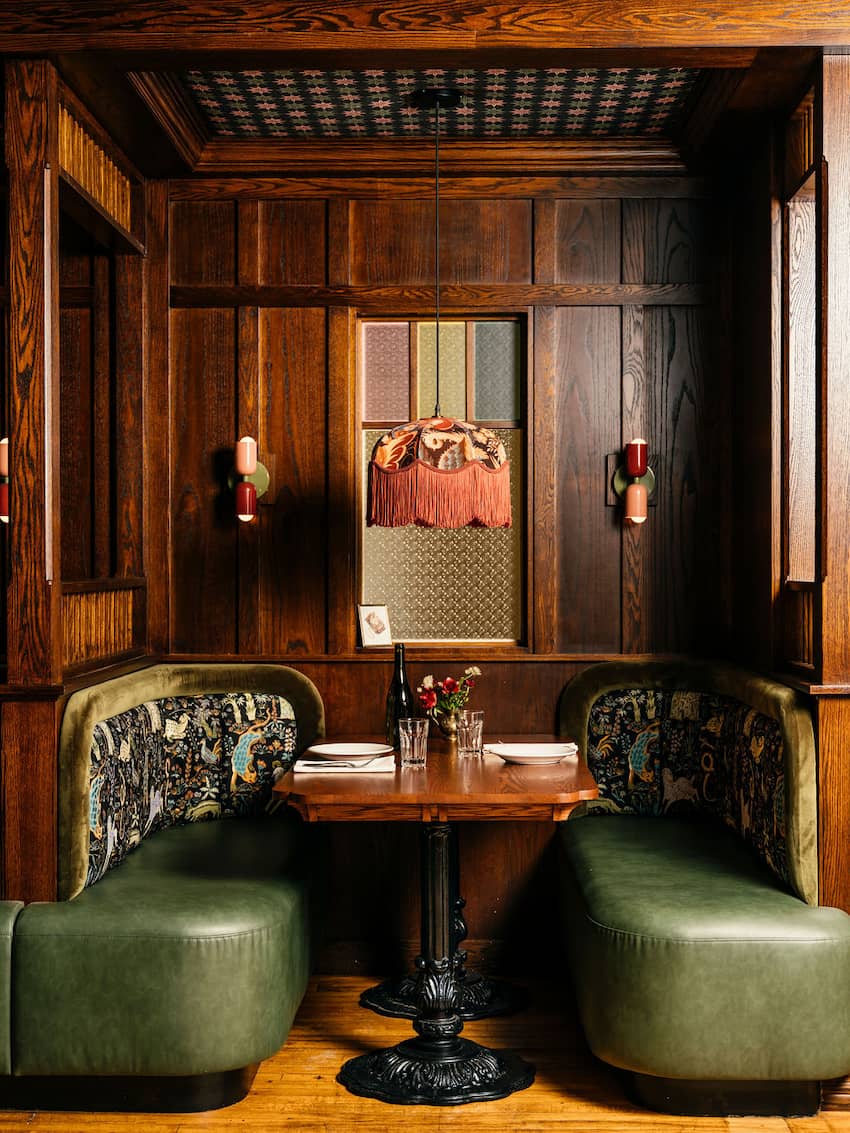 A cozy wooden booth with green upholstered seating, patterned accents, and a fringed vintage lamp.