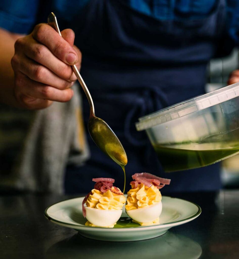 Chef pouring sauce over deviled eggs topped with pickled onions.