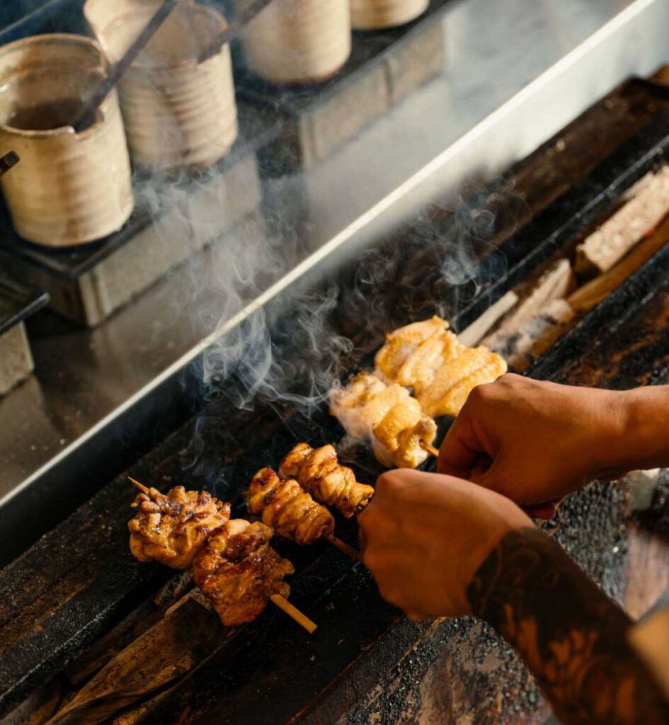 Chef grilling skewers of chicken over smoky charcoal bbq.