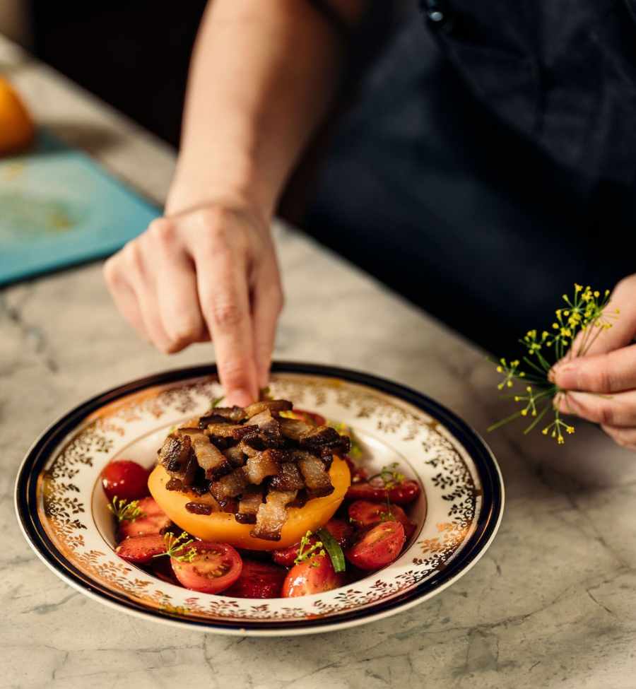 Garnishes being placed on a halved tomato with bacon